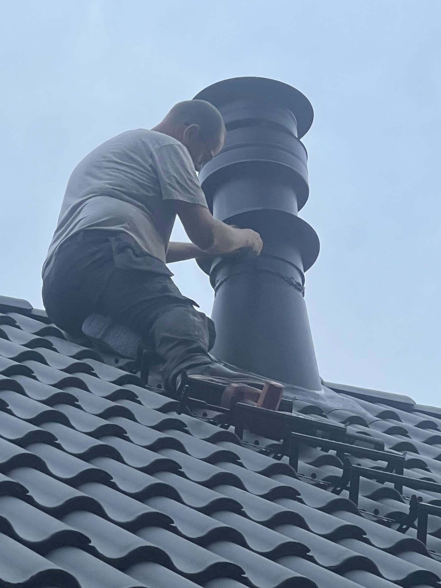 Fagperson inspiserer skorstein på tak under rehabilitering i enebolig i Skjeberg.