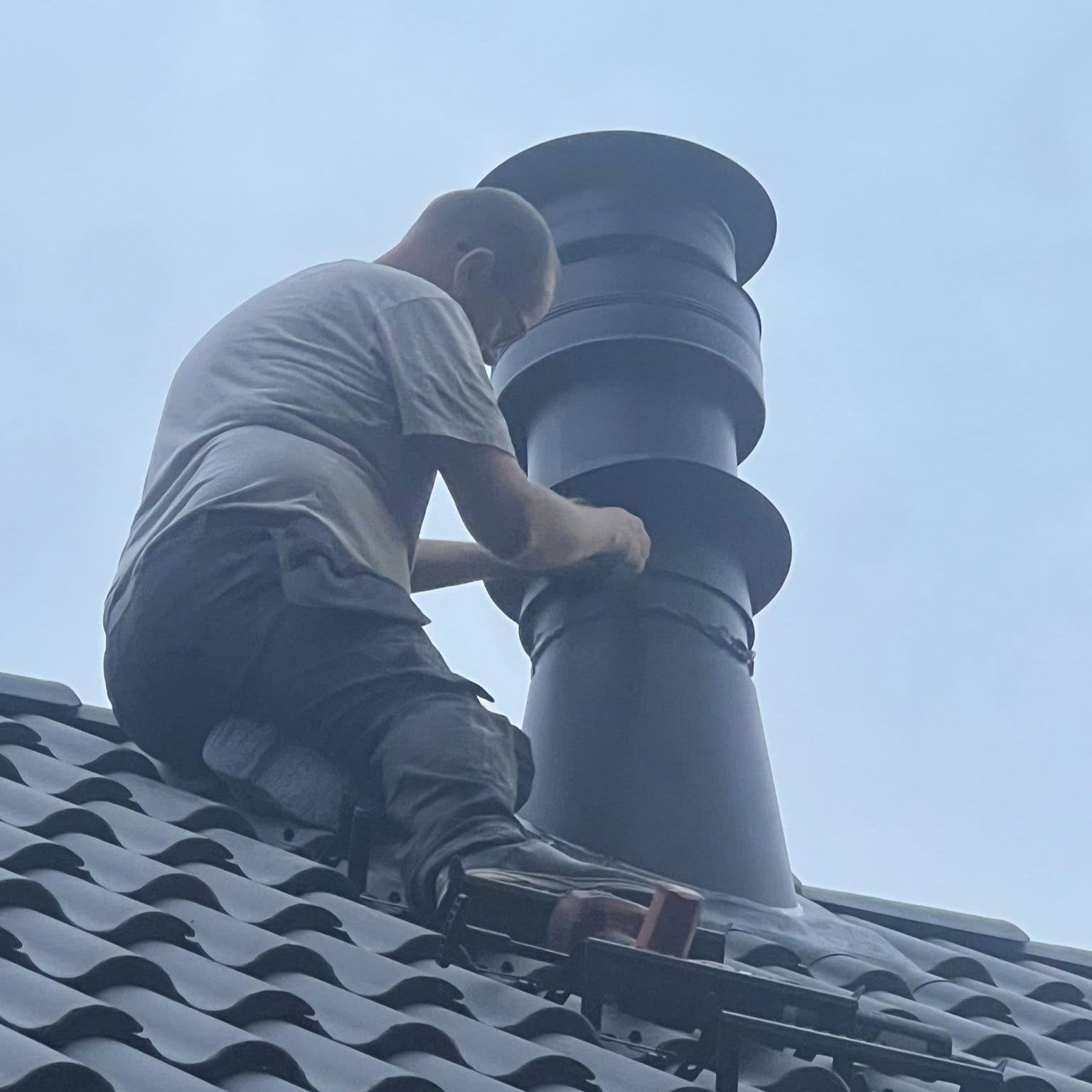 Fagperson inspiserer skorstein på tak under rehabilitering i enebolig i Skjeberg.